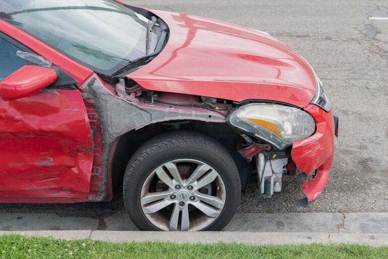 A car with visible bumper and fender damage after a traffic accident, representing modern post-fender bender repair and insurance choices. 