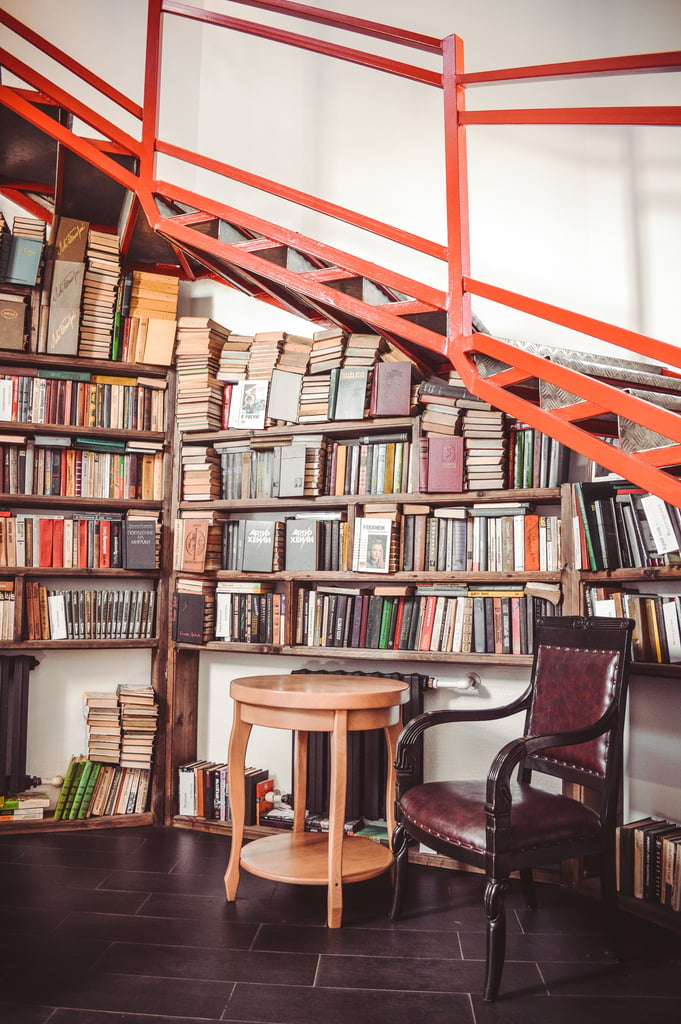 A bookshelf tucked underneath a staircase with an armchair.