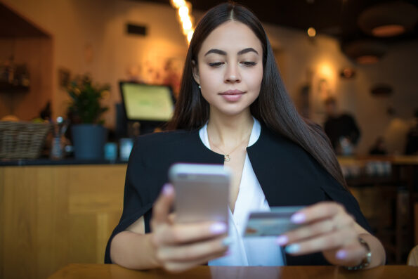 Confident business woman online payment via mobile phone using credit debit card while relaxing in restaurant. Female online shopping store via cellphone, resting in coffee shop during recreation time