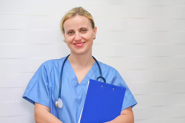 Doctor, nurse with stethoscope and folder in hand in hospital. Doctor or nurse holding a folder of information. Smiling doctor or nurse holding folder. Image of a trainee doctor looking at the camera.