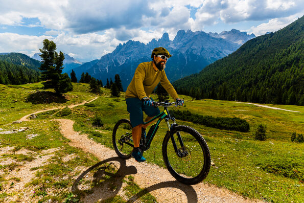 Single mountain bike rider on electric bike, e-mountainbike rides mountain trail. Man cycling on bike in Dolomites mountains. Cycling e-mtb enduro trail track. Outdoor sport activity.