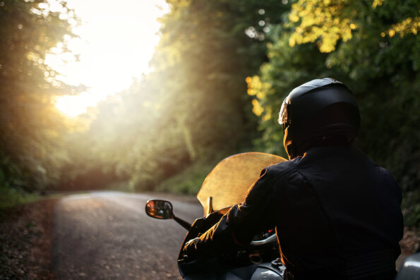 Biker with his motorcycle on street, preparing for the ride. Motorcycle guy with motorcycle on the road. Driver riding motorcycle on the road through forest.The view over the handlebars of motorcycle.