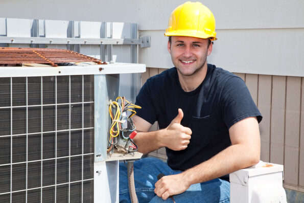 Air conditioning repairman working on a compressor and giving a thumbsup.