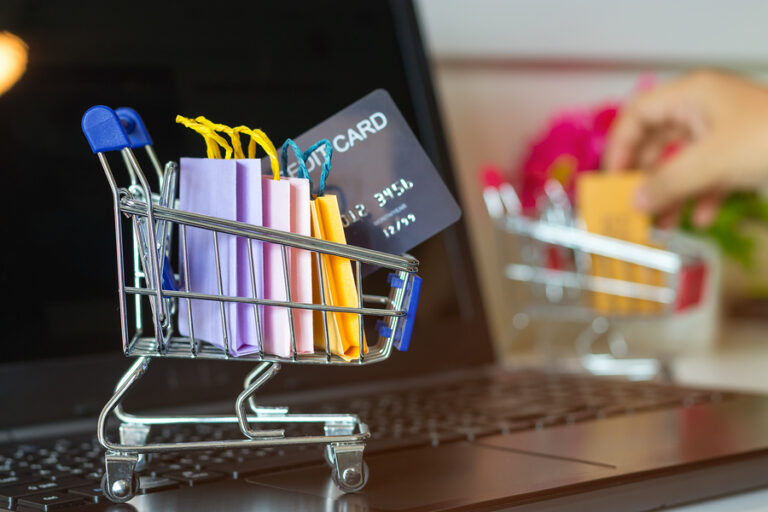 Paper shopping bag with text online shopping and hand holding mock-up of credit card on laptop keyboard. Consumer can buy product anywhere anytime using internet. Online shopping and ecommerce concept