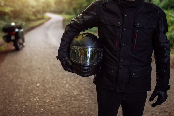 Motorcycle guy in raiders clothes, gearing up. A young men stands near an motorcycle in nature during sunset. Biker with motorcycle on the road. Motorcycle and safe driving. Helmet and motorcycle.