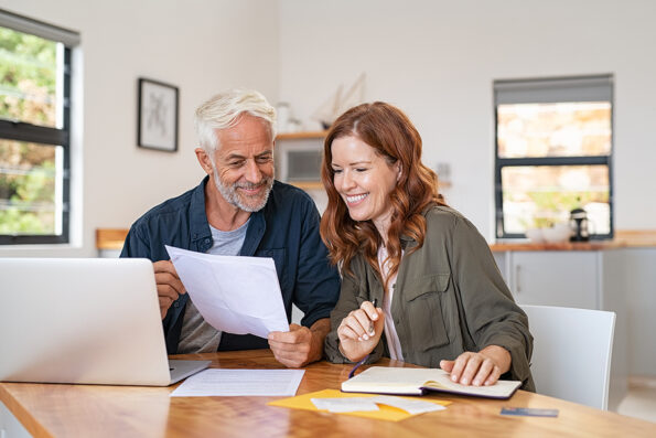 Mature smiling couple sitting and managing expenses at home. Happy senior man and mid woman paying bills and managing budget. Middle aged couple checking accountancy and bills while looking receipt. bills