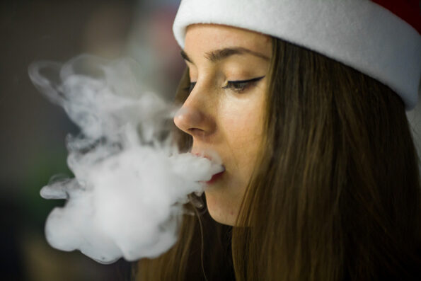 Vape teenager. Young pretty white caucasian girl in a hat of Santa Claus smoking an electronic cigarette in vape bar. Bad habit that is harmful to health. Vaping activity.