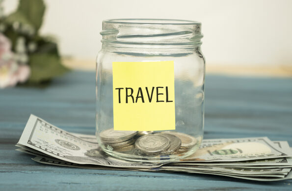 Travel budget - vacation money savings in a glass jar on world map. Travel budget concept. Money saved for vacation in glass jar on world map background, copy space. Banknotes and coins for adventure