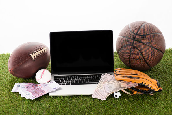 laptop near sports balls, baseball glove, euro and dollar banknotes on green grass isolated on white, sports betting concept