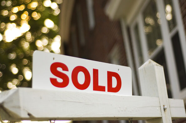 real estate sold sign with red brick building and trees blurry in the background