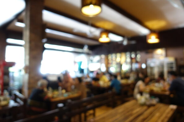 blurred image of group of people of enjoy talking and eating some food with their family on table in restaurant. vintage tone and light effect. Abstract restaurant interior for background