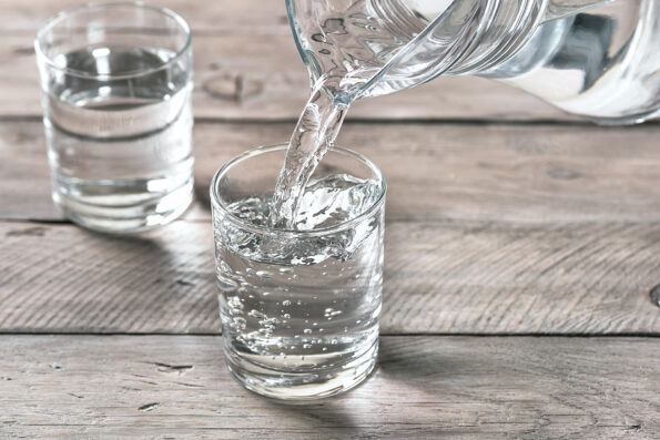Water pouring into glass. Glass of water on wooden table, selective focus, close up. Clear purified water for drink.