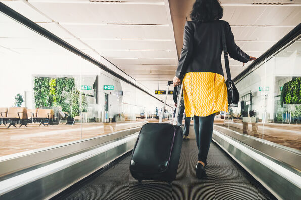 Woman traveller with travel suitcase or luggage walking in airport terminal walkway for vacation travel abroad. concept of travel around world, tourism. Brunette in yellow skirt goes on escalator.