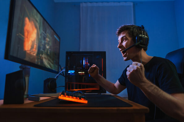 Cybersport young pro gamer happy with winning the game, feel exited, show YES hand gesture, celebrates victory in online game competition. Side view. Guy playing video game at home in his room