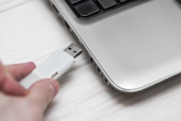 Plugging removable flash disk memory into laptop USB slot. Man hand inserting USB flash drive into laptop computer on wooden white background. Copying data from flash drive to laptop computer storage