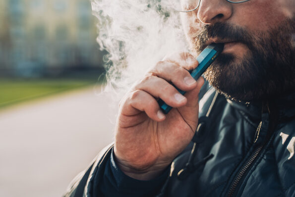 vaping Man smokes new Vape Pod System, inhales and exhales vapor of electronic cigarette, vaping concept, selective focus, toned