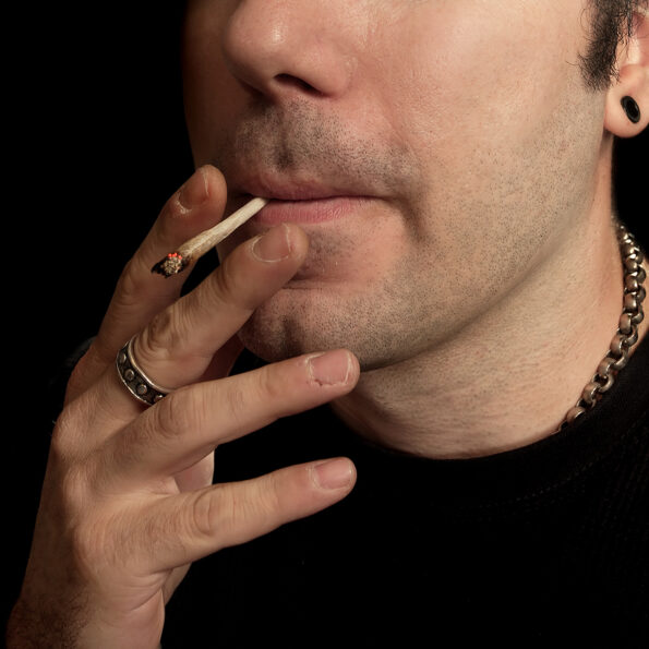 A close cropped image of a man smoking a marijuana joint.