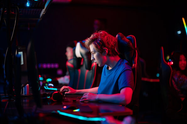 Training bootcamp for professional esports players. Young cyber-athletes play an online shooter game. Glowing keyboard, neon light.