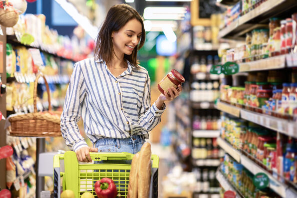 food brand Portrait Of Smiling Woman With Shopping Cart In Supermarket Buying Groceries Food Walking Along The Aisle And Shelves In Grocery Store, Holding Glass Jar Of Sauce, Choosing Healthy Products In Mall