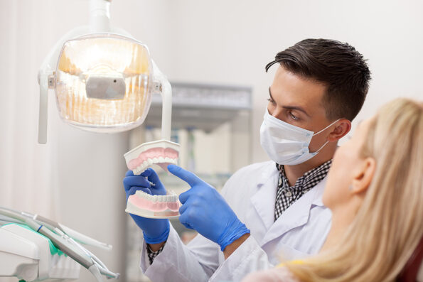 Male dentist explaining his female patient about teeth care, showing her dental mold. Professional dentist working at his office. Woman visiting dentist for oral checkup. Communication, treatment
