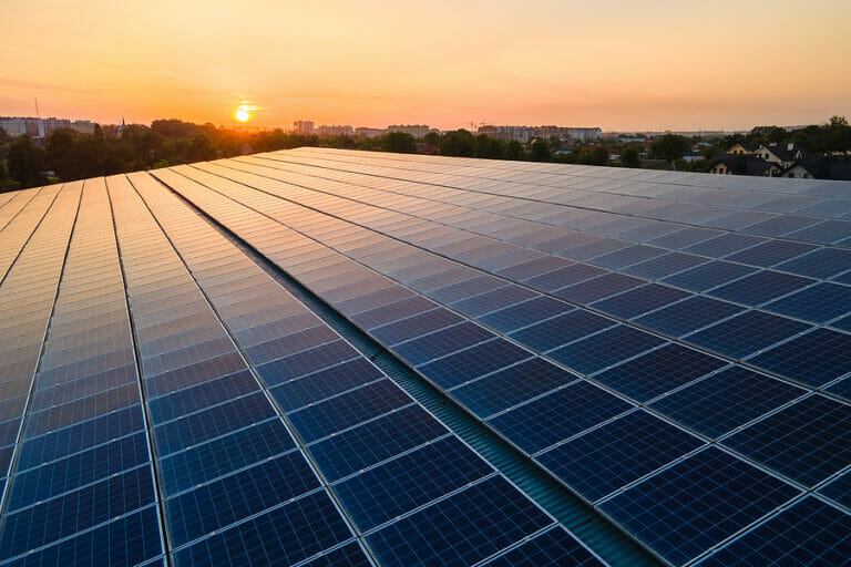 Blue photovoltaic solar panels mounted on building roof for producing clean ecological electricity at sunset. Production of renewable energy concept.