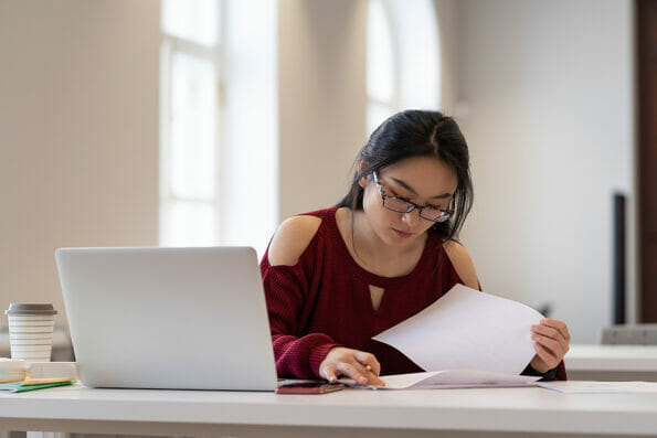 Concentrated student girl or young businesswoman busy with documents working in campus open space. Young asian woman of 20s studying read documents preparing for exam or test in university or college