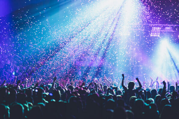 A crowded concert hall with scene stage lights, rock show performance, with people silhouette, colourful confetti explosion fired on dance floor during a concert festival