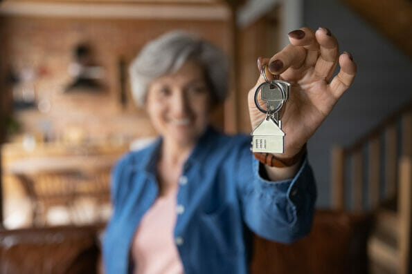 Happy elderly female homeowner pose in country cottage hold keys