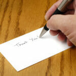 Person writing thank you note with pen on card