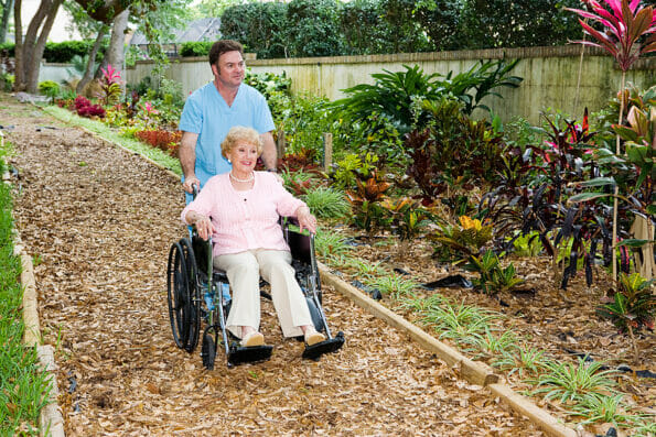Nursing home orderly pushing a disabled senior woman through the garden.