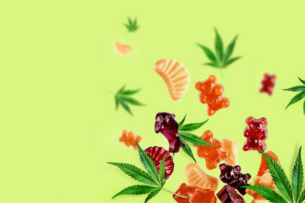 Colored gummies fly along with cannabis leaves. Chewing candies, gummies with CBD oil and THC. Colorful creative background, minimalism.