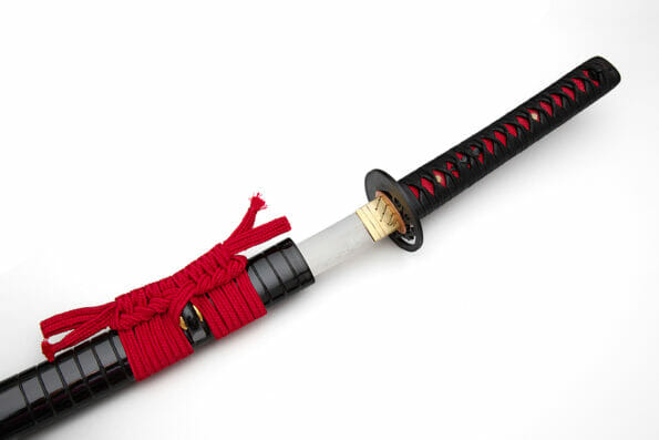 Japanese sword with red cord steel fitting and shiny black scabbard on white background. Selective focus.