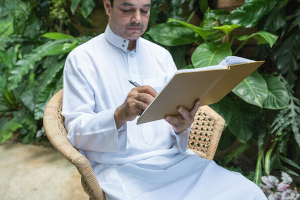 Saudi muslim man dress hijab sitting and writing on textbook,freelance business concept.