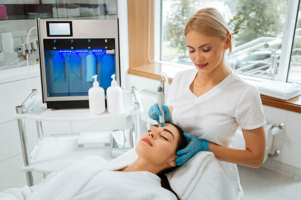 Professional skilled female cosmetologist doing hydrafacial procedure