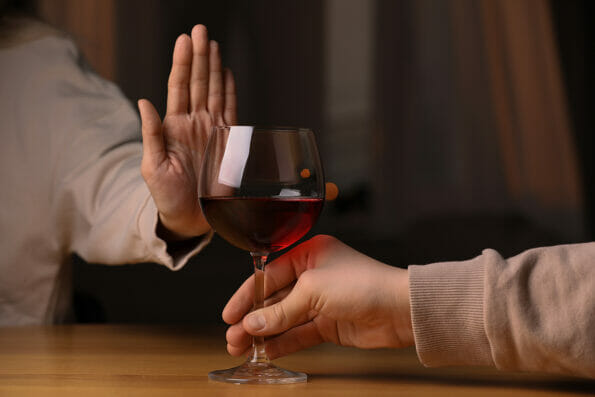 Woman refusing to drink red wine indoors, closeup. Alcohol addiction treatment