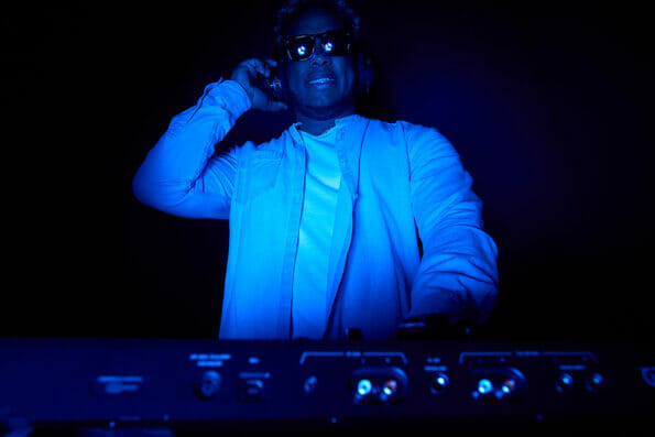 African-American DJ puts on music in a dark room. Color music for a party. DJ wearing headphones and glare sunglasses puts on music at a party.