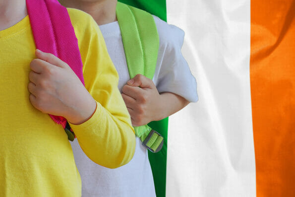 Two children with satchels background of Ireland flag. The concept of raising and educating children in Ireland