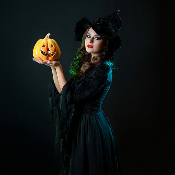 beautiful witch in a pointed hat Holding a pumpkin with a laughing face, Jack lantern. Halloween party, witches  Sabbath. Young beautiful brunette in witch costume,