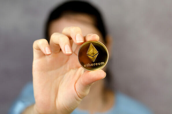 Ethereum coin in a female hand close-up. Unrecognizable woman holding ethereum in front of her face. Cryptocurrency