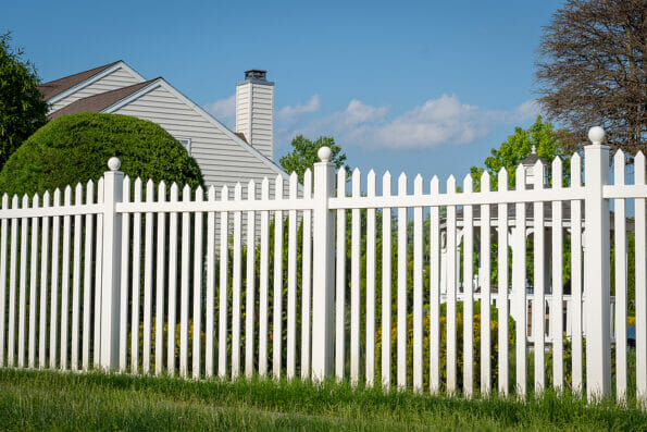 White vinyl fence in a cottage village tall thuja bushes behind the fence fencing of private property grass plastic