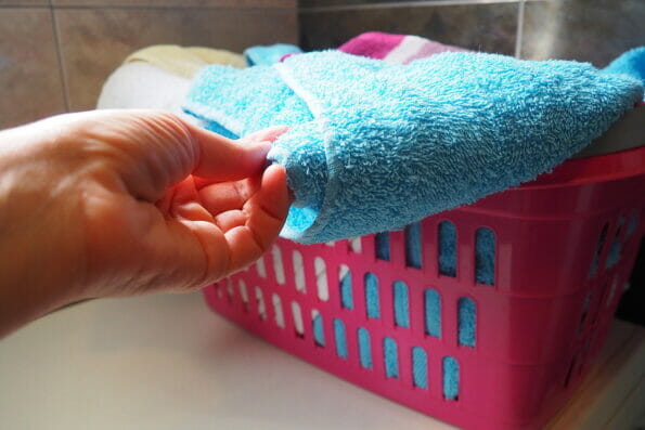 A woman's hand is feeling a cotton colored towel from a basket with dirty laundry. Laundry sorting and washing. Laundry room or bathroom. Housekeeping. Pink and blue terry towels