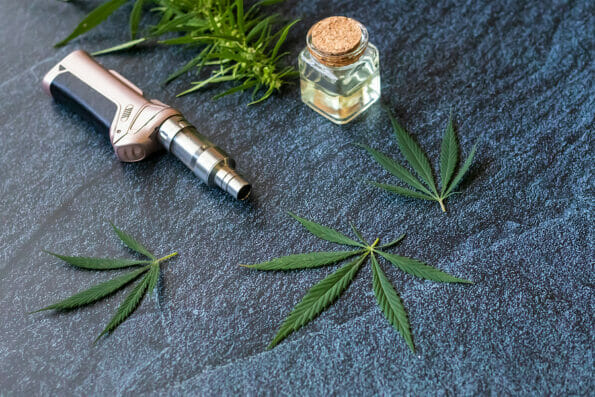 Close-up Vaping Cannabis THC Oil Extract in Cartridge Isolated on Dark Background with Marijuana