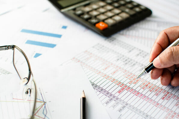 Financial accounting, work at home, Close-up Man's hand holding a pen examining accounting numbers. Numbers on paper and calculator, Many numbers, graph, pencil, glasses on paper, Blurred background.