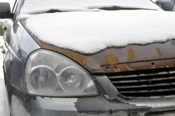 Rusty hood of an old car covered with snow. Auto junk.