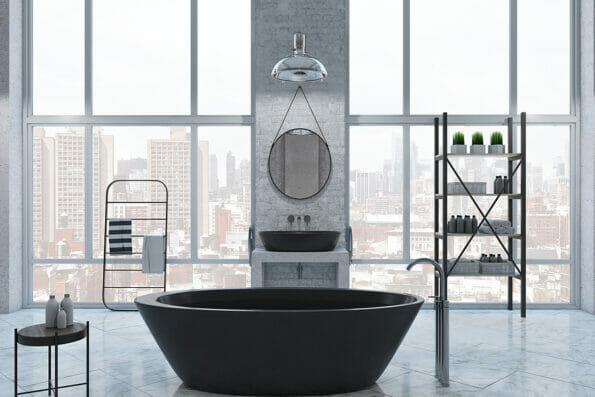 Front view on modern black bath in big sunlit loft style bathroom with metallic furniture, round mirror on concrete wall and city skyline view from panoramic windows. 3D rendering
