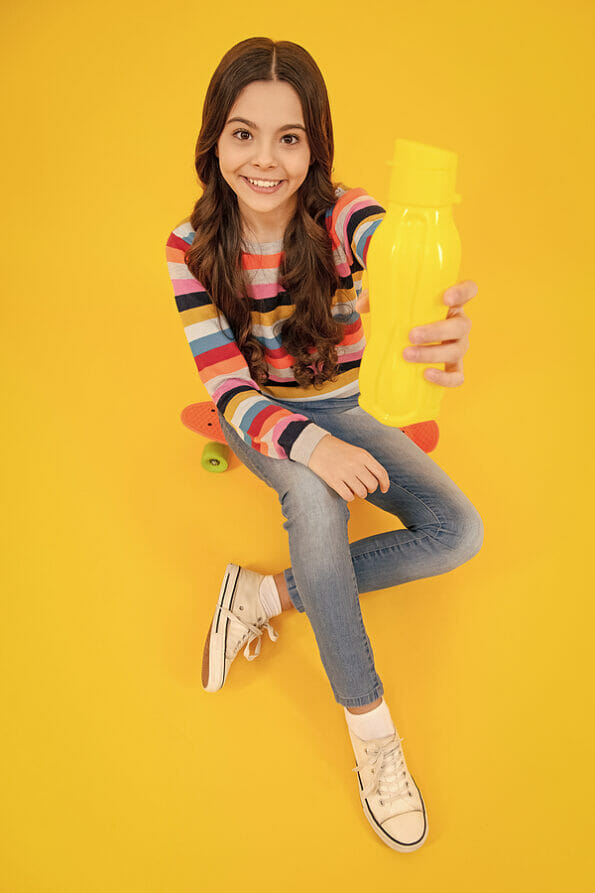 Teenage girl hold water bottle isolated on yellow background. Water bottle and healthy life. Health and water balance. Drink and beverage concept. Happy teenager, positive and smiling emotions.