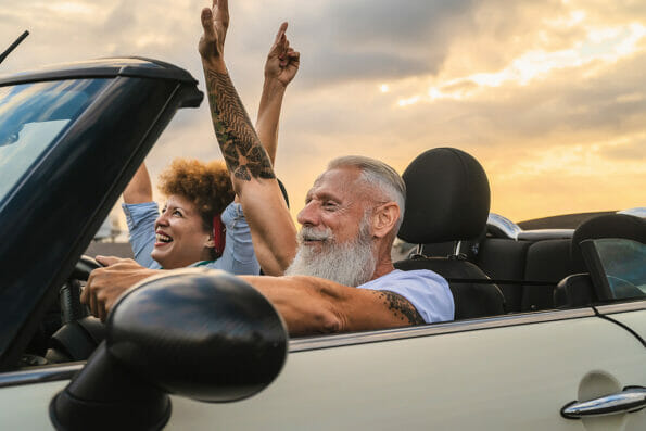 Happy senior couple having fun driving on new convertible car - Mature people enjoying time together during road trip tour vacation - Travel people lifestyle concept