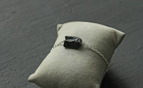 Black tourmaline, sherl bracelet on silver chain. Bracelet made of stones on hand from natural stone Black tourmaline on black concrete modern background. Magic jewelry, lithotherapy, stone therapy.