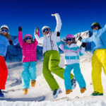 Family skiing and jumping together on a sunny mountain slope during winter vacation.